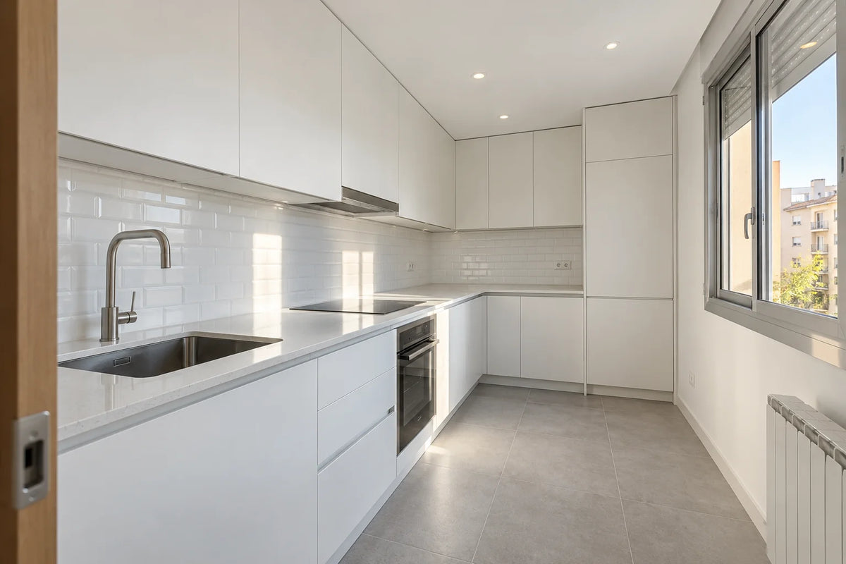 Cocina reformada en un piso de Madrid con muebles blancos sin tiradores, encimera de cuarzo y suelo porcelánico gris claro
